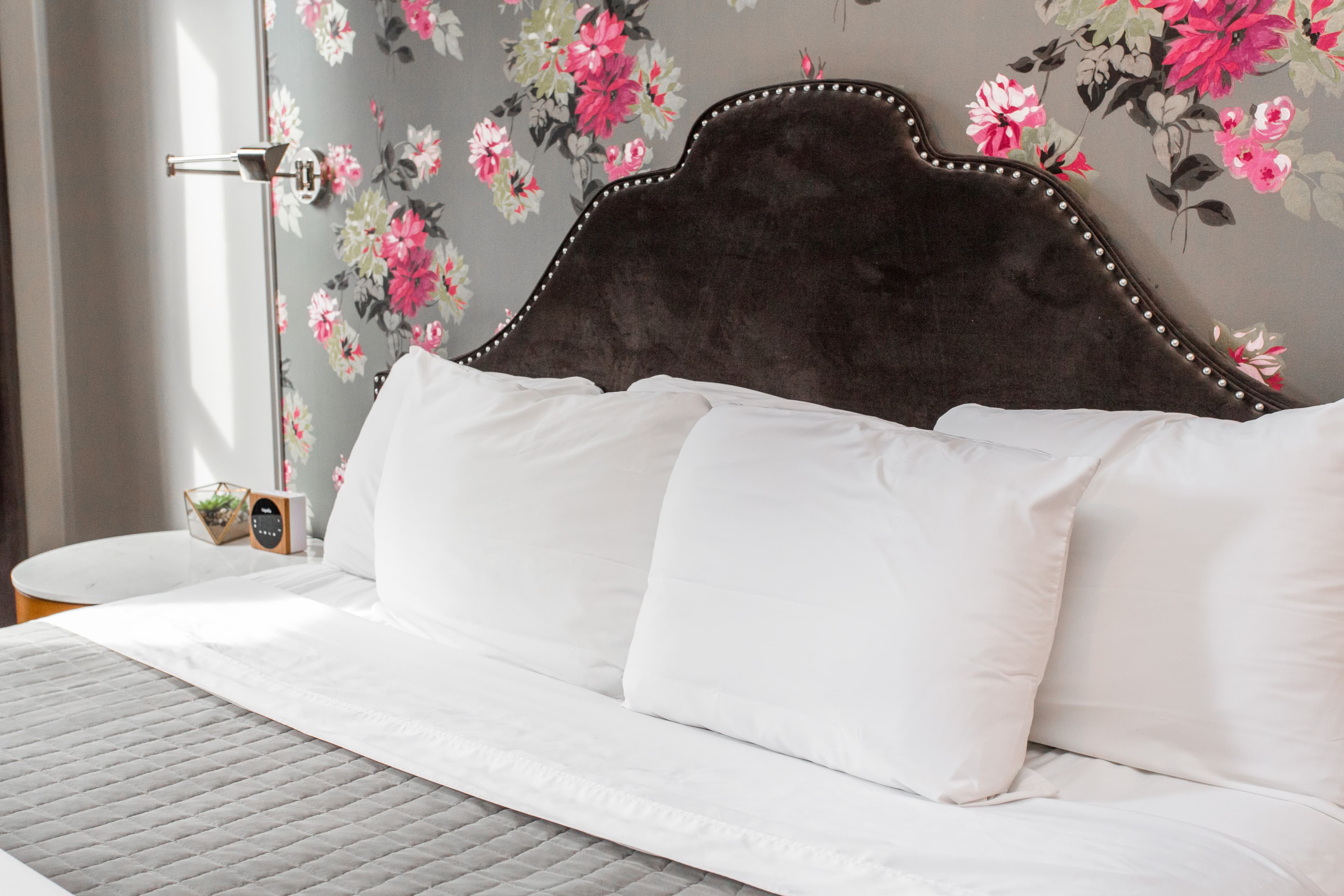 The pillows, plush headboard and flowered nightstand by the bed