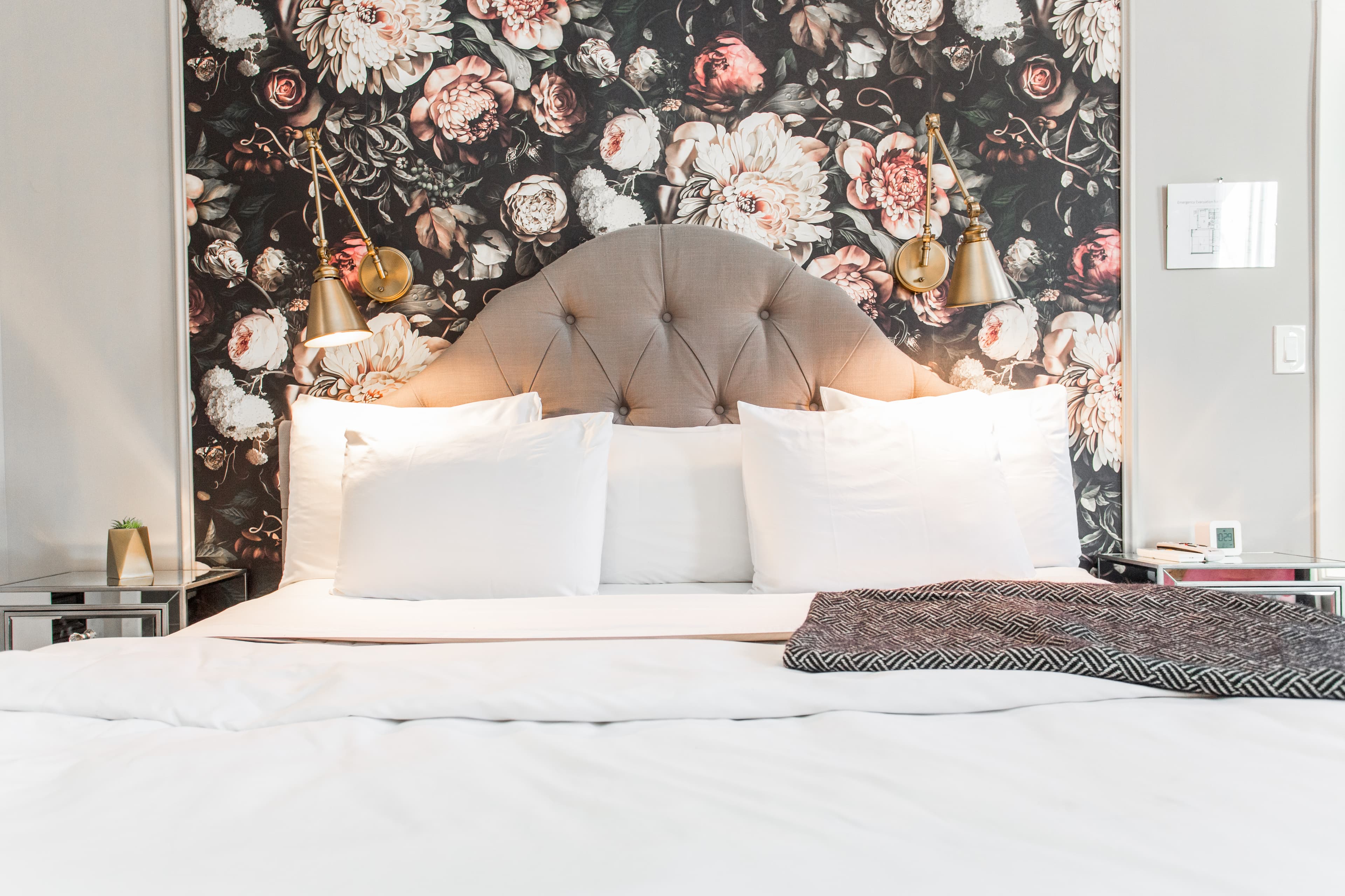 Sprawling Wolcott King bed with padded headboard, flowers on the nightstand and pleasant floral wallpaper