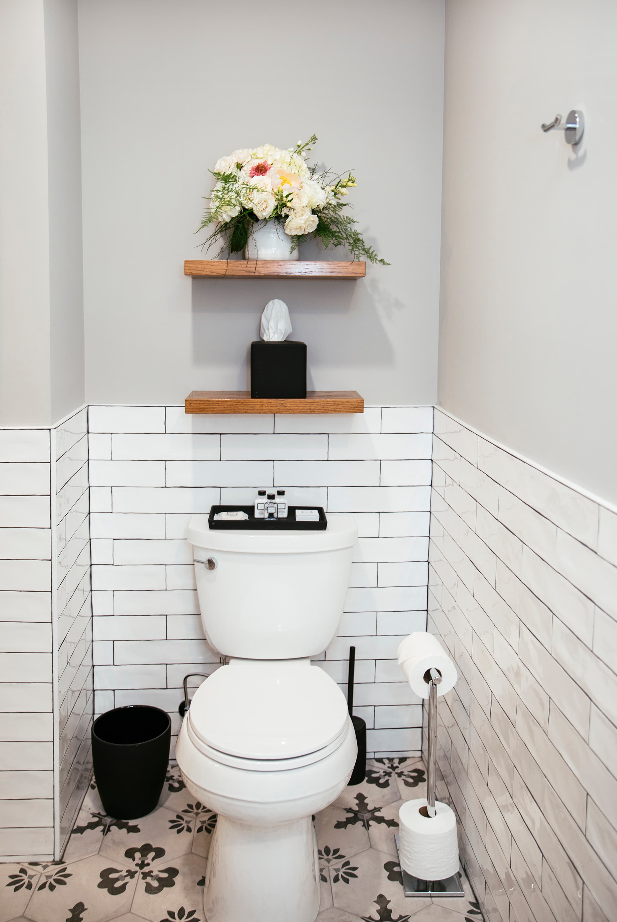 Wolcott's toilet and wooden wall shelves arranged with complimentary toiletries, tissues and decorative flowers