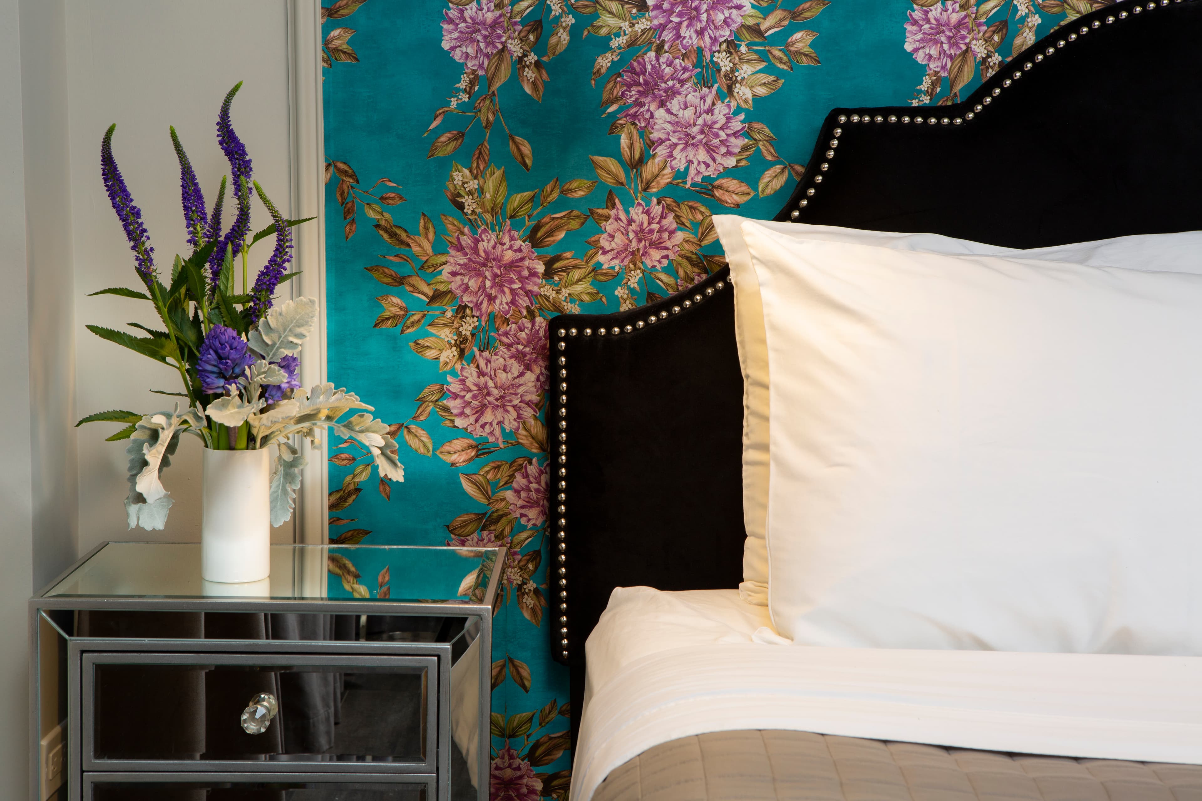A closer image of the bed's fluffy pillows and the flowers on the bedside table.
