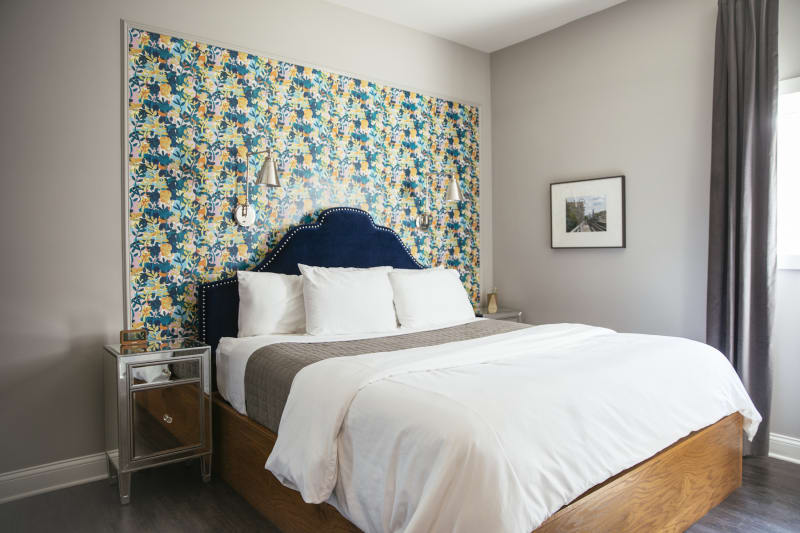 Ellen's king-size bed, sunlit window with soft floor-length curtain, and cool tropical wallpaper.