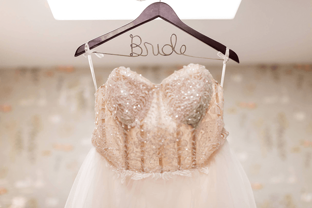 A beautifully beaded wedding dress hangs on a decorative hanger labeled "Bride."