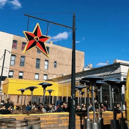 A red and black star sign hangs above a bustling outdoor dining area under a bright blue sky.
