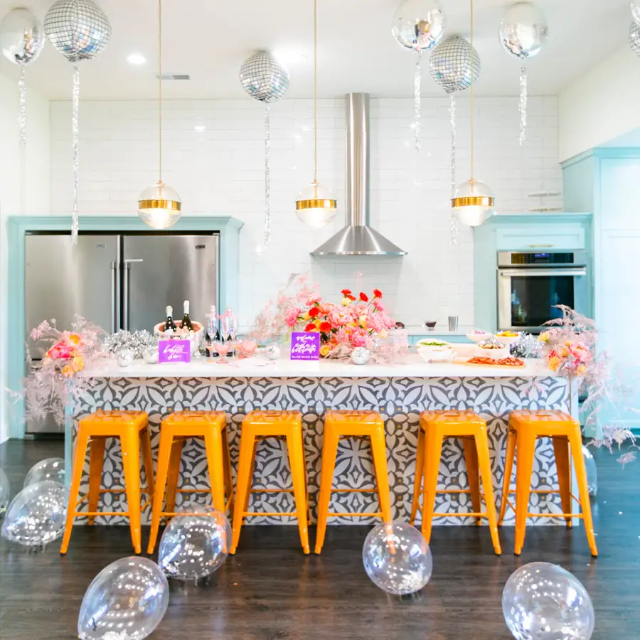 Modern kitchen with orange stools, floral decorations, and mirrored balloons.