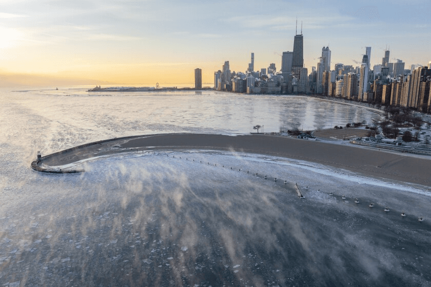 Aerial view of a frozen Lake Michigan shoreline with a skyline of Chicago at sunrise.