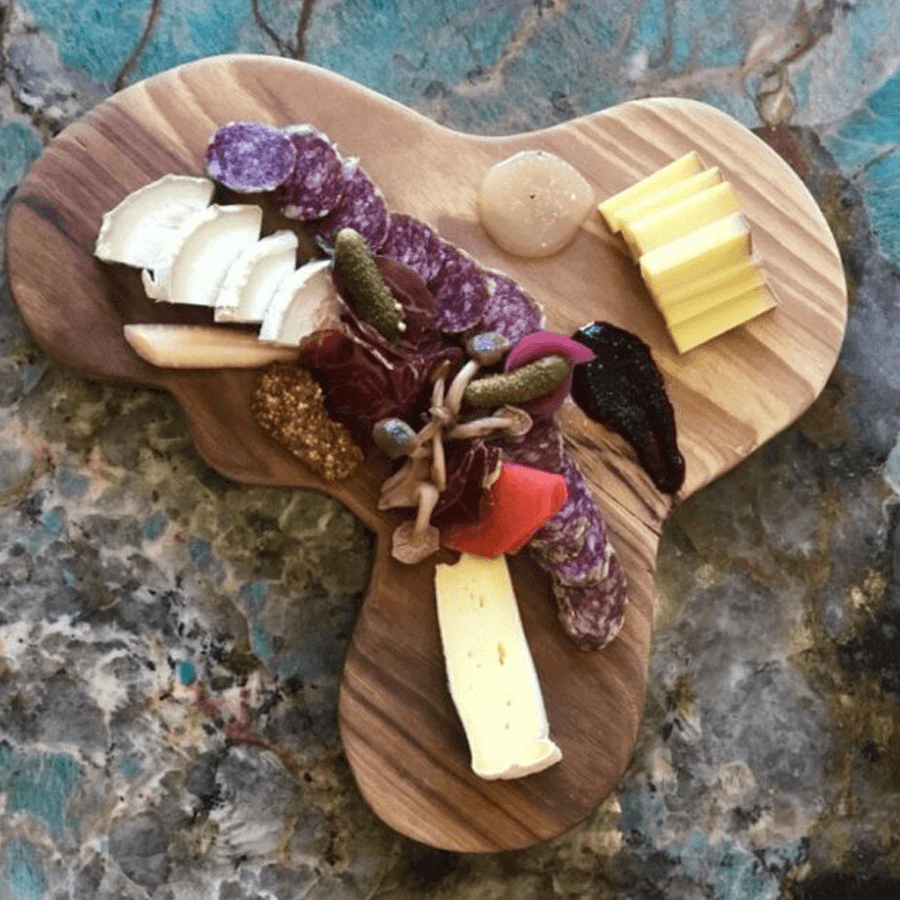 A wooden cheese board featuring assorted cheeses, meats, pickles, and condiments.