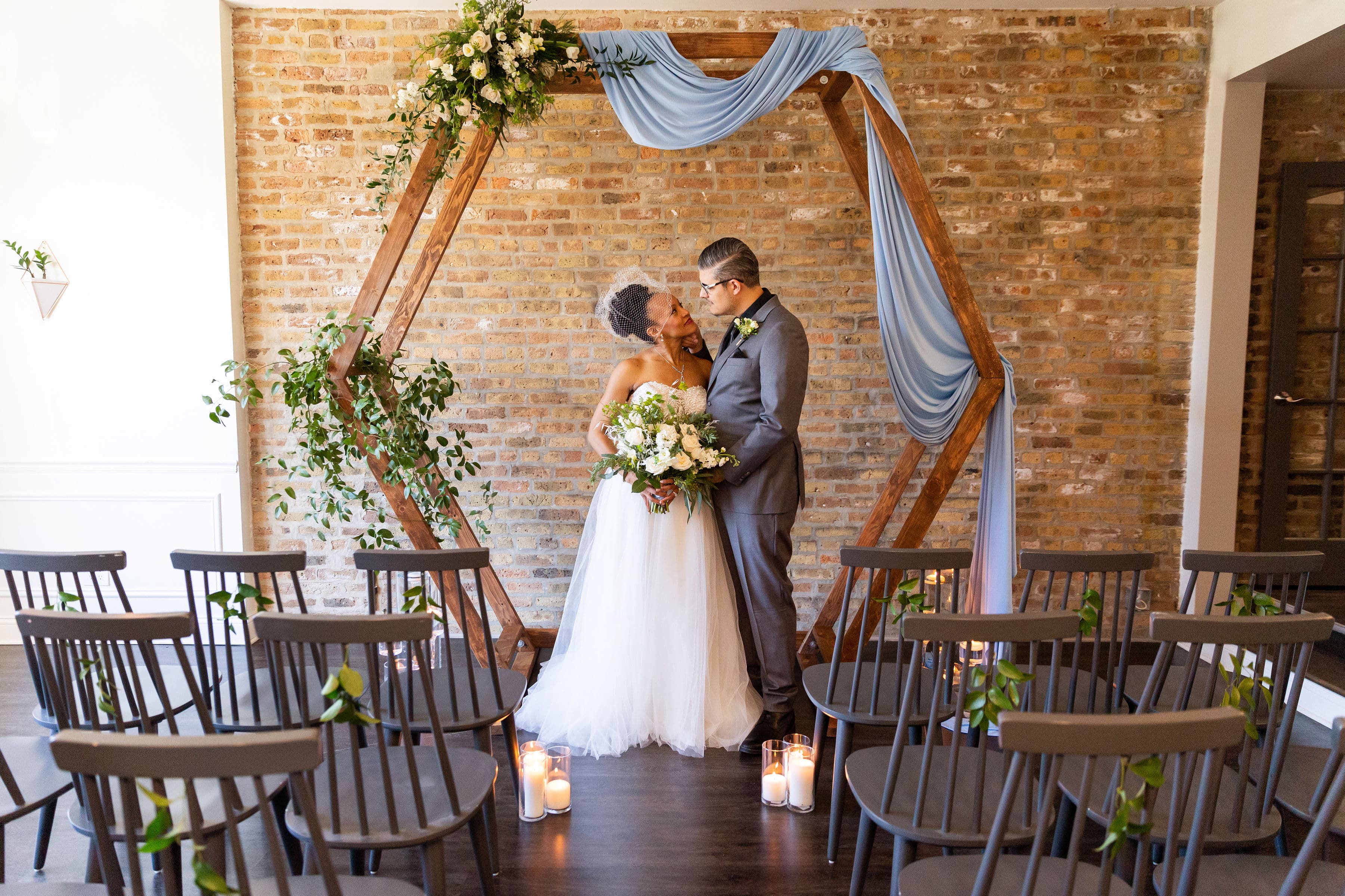 A bride and groom share a kiss under a decorated arch in an intimate wedding venue. A bride and groom share a kiss under a decorated arch in an intimate wedding venue.
