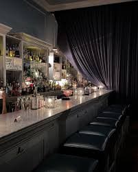 A dimly lit bar featuring a long marble countertop and shelves lined with various bottles.
