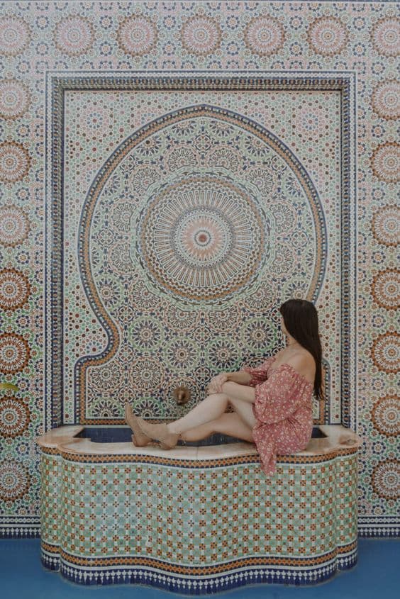 A person sits on a decorative basin in front of a vibrant, patterned tiled wall. A person sits on a decorative basin in front of a vibrant, patterned tiled wall.