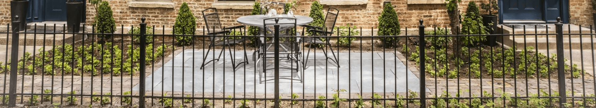 A small outdoor seating area enclosed by a black fence, featuring a round table and chairs.