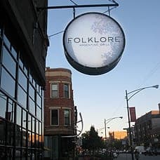 Round sign reading "FOLKLORE" outside a building at dusk.