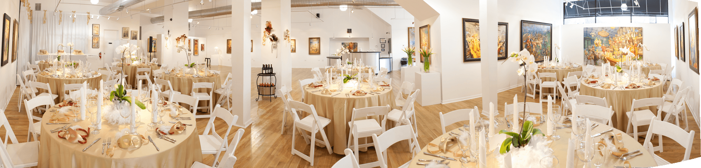 Gold linen covered round dining tables with white folding chairs, wood floors and framed art on the walls