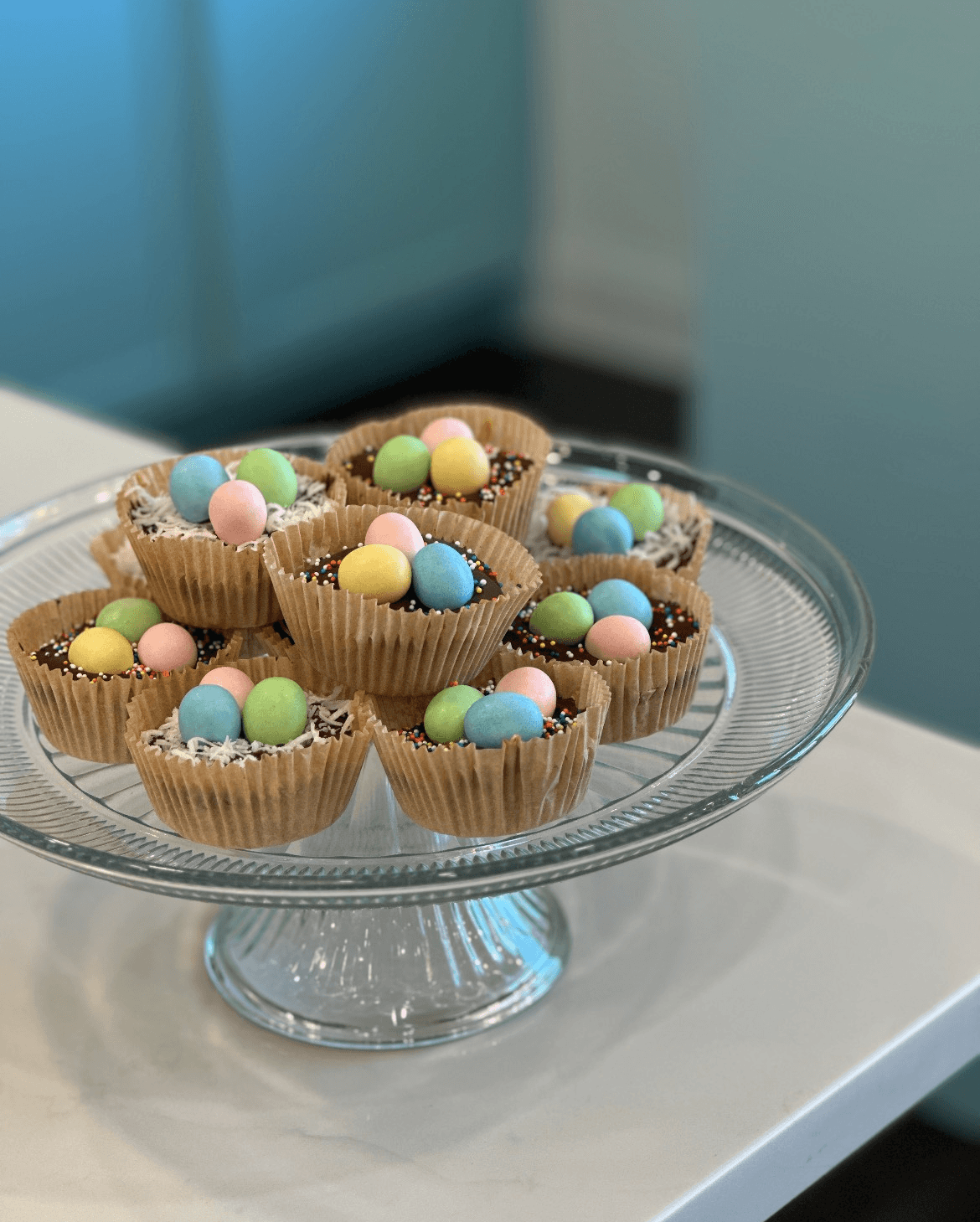 A glass platter holds chocolate cups decorated with pastel-colored candy eggs. A glass platter holds chocolate cups decorated with pastel-colored candy eggs.