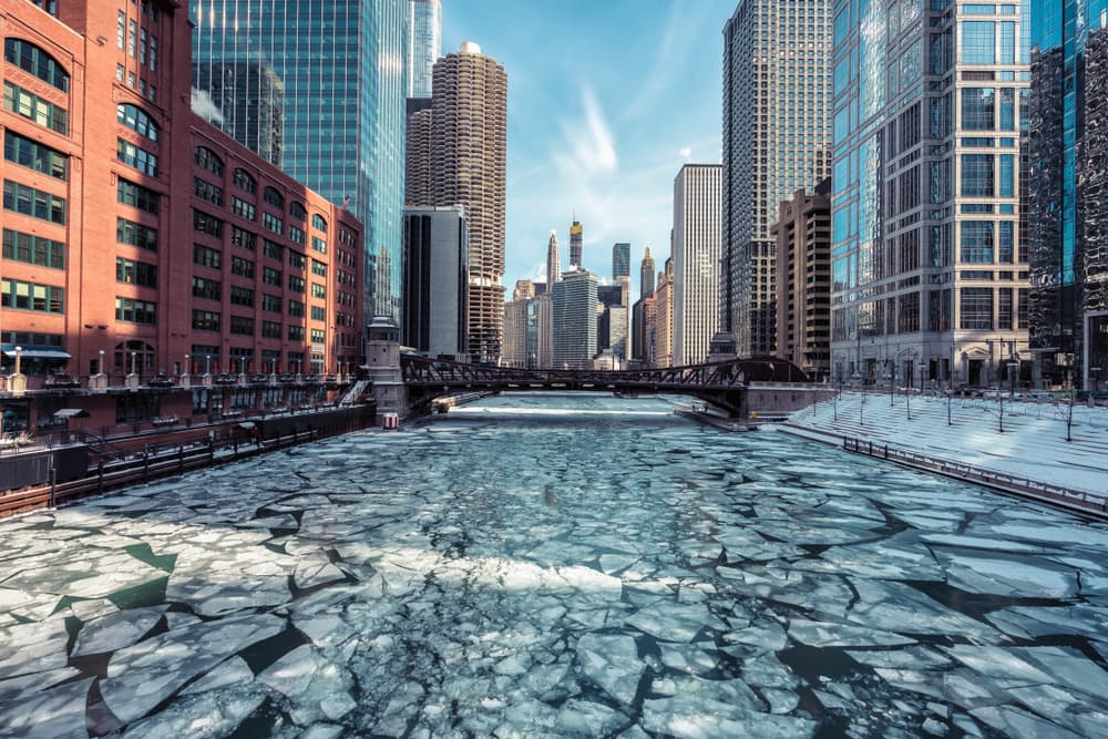A frozen river flows through a cityscape of tall buildings under a clear blue sky. A frozen river flows through a cityscape of tall buildings under a clear blue sky.