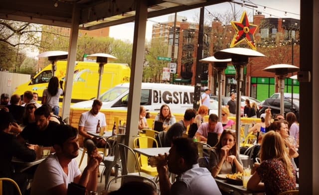 A busy outdoor dining area filled with patrons enjoying food, with a food truck visible in the background. A busy outdoor dining area filled with patrons enjoying food, with a food truck visible in the background.
