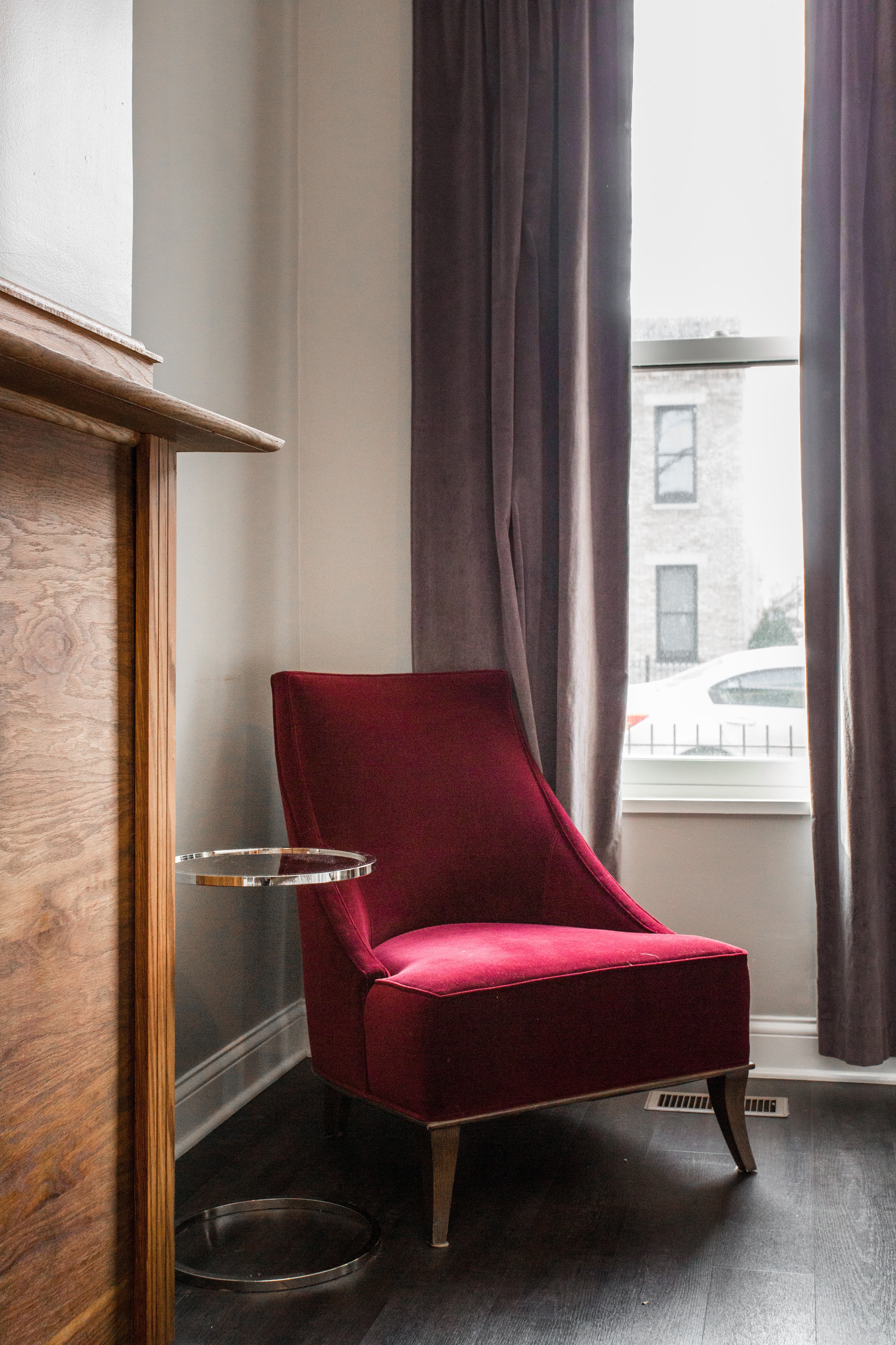 A red accent chair sits beside a small glass side table in a well-lit room.