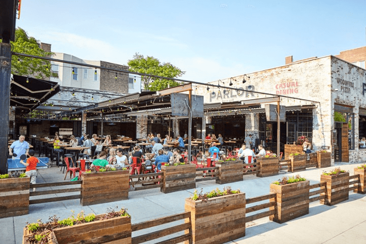 A bustling outdoor restaurant with people dining at wooden tables under string lights.