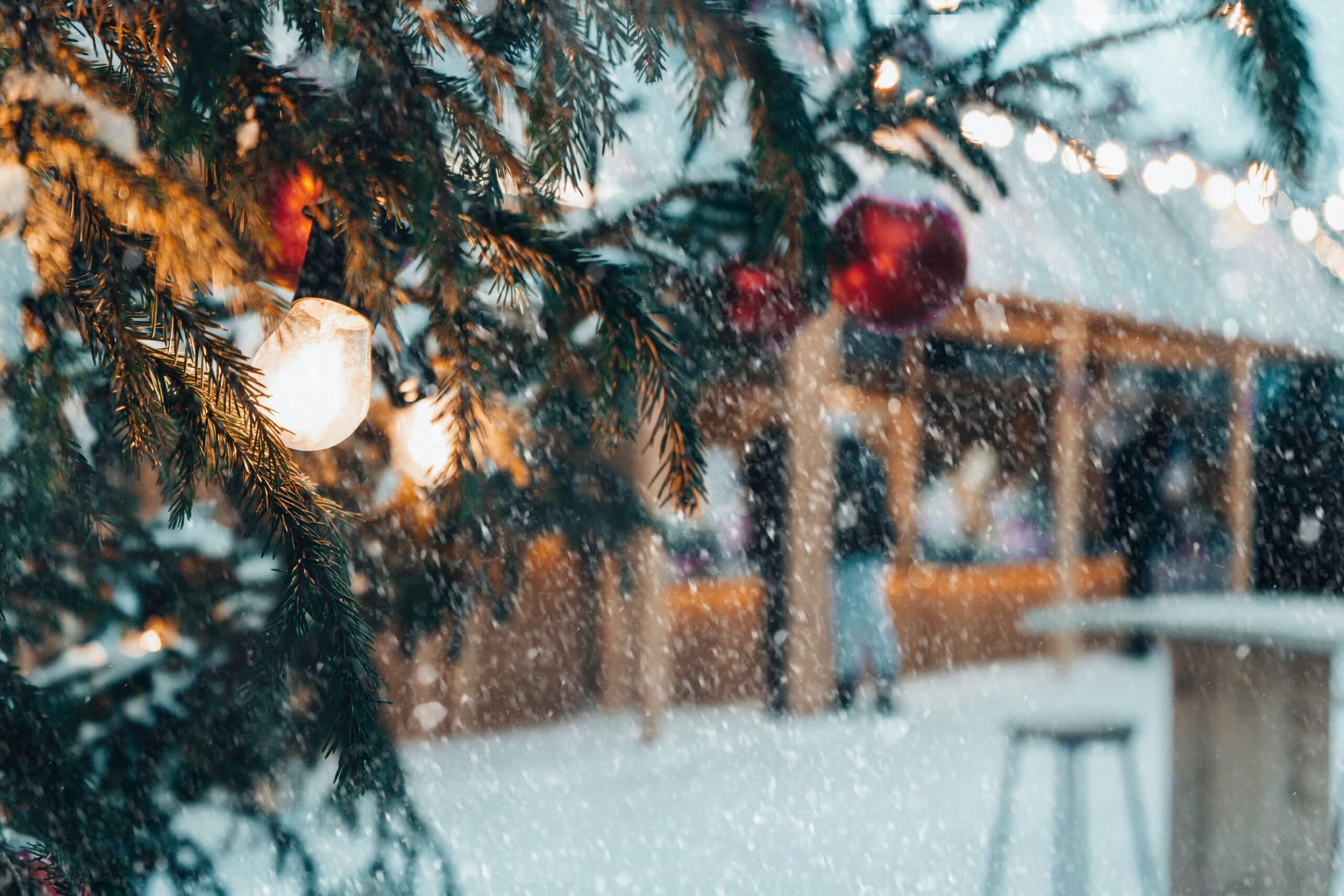 A snowy scene featuring a decorated evergreen tree with lights and ornaments, set against a blurred market backdrop. A snowy scene featuring a decorated evergreen tree with lights and ornaments, set against a blurred market backdrop.