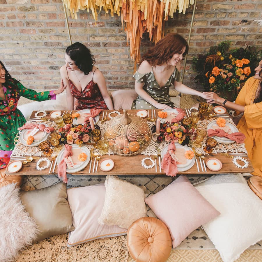 A vibrant table setting with four women sharing a joyful moment surrounded by floral decorations and colorful dishes.