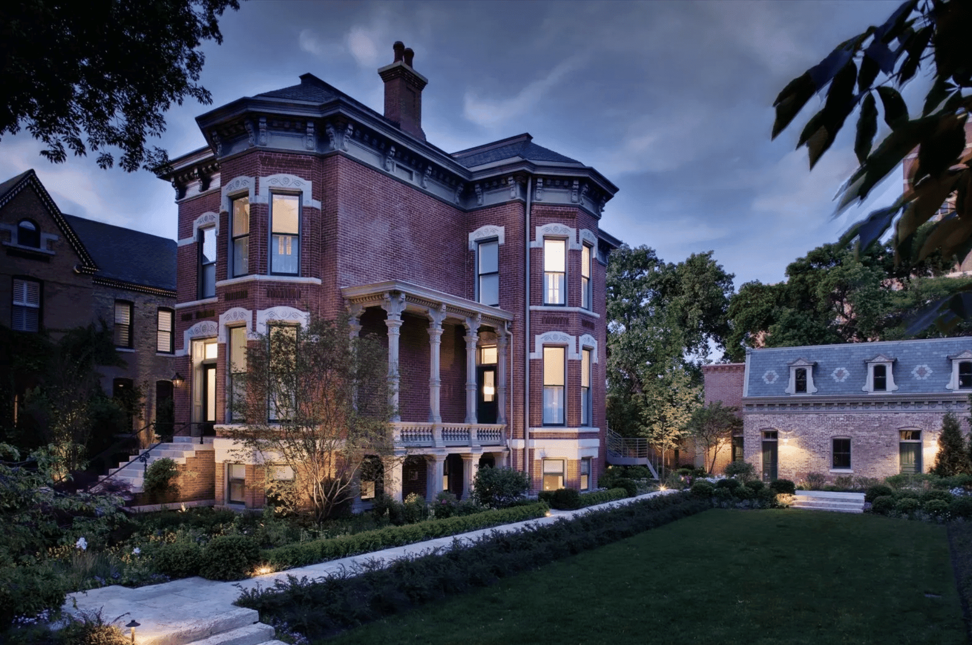 A grand brick mansion with columns surrounded by a lush garden at dusk. A grand brick mansion with columns surrounded by a lush garden at dusk.