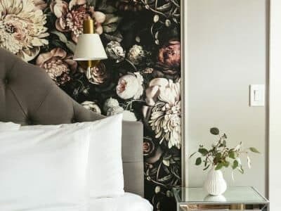 A cozy bedroom with a floral accent wall and a bedside table.