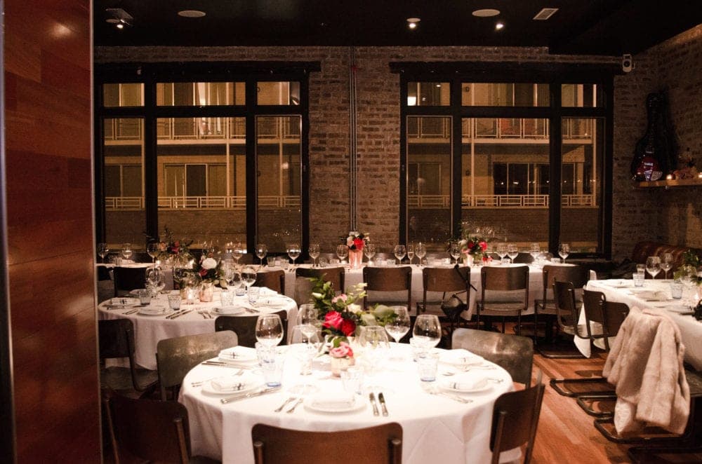 Elegant dining setup with white tablecloths, wine glasses, and floral centerpieces in a warmly lit restaurant.