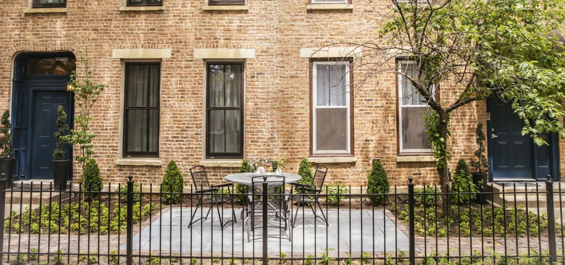 A small outdoor seating area with a round table and chairs, framed by a brick wall and greenery.