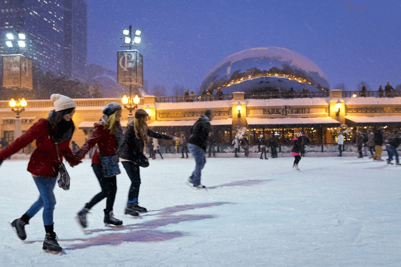 A group of people ice skating at an outdoor rink in a snowy urban setting.