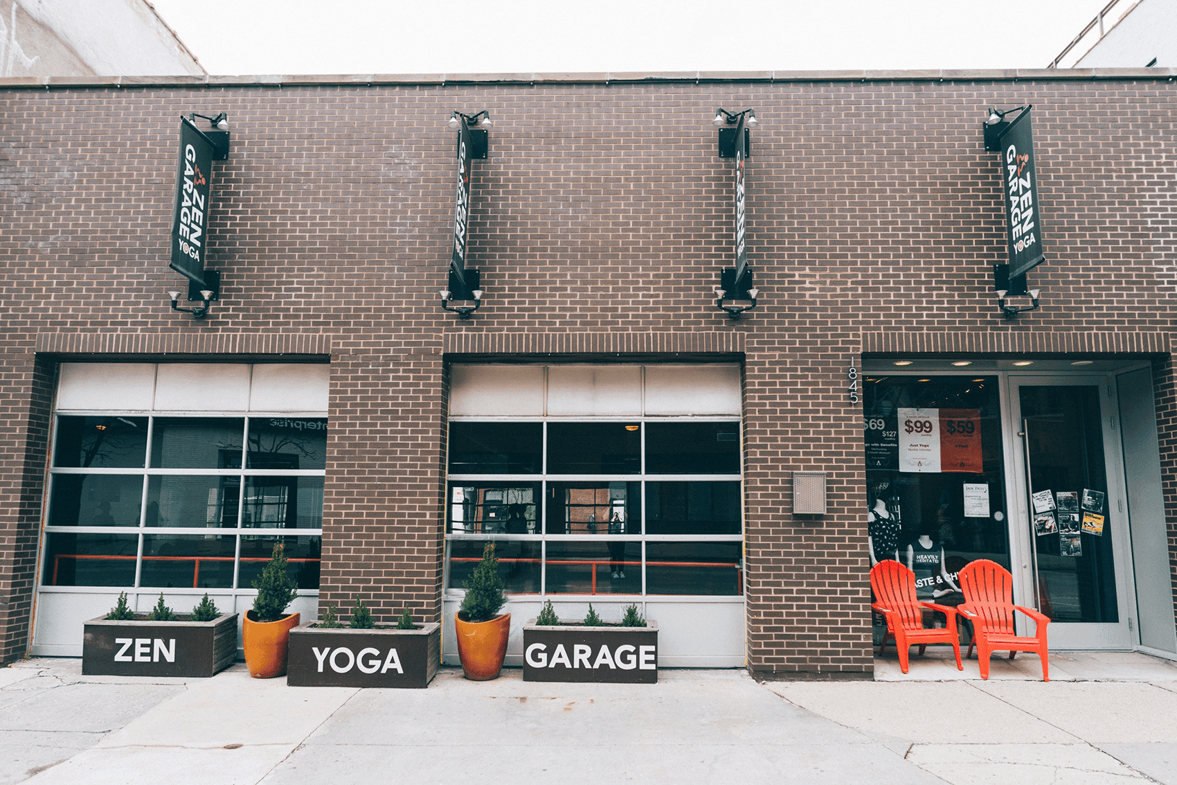 A brick building with signs reading "Zen," "Yoga," and "Garage," featuring orange chairs outside.
