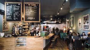 A cozy café featuring a wooden counter, menu boards, and patrons enjoying their time.