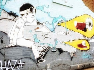 A mural depicting a boy in goggles, sitting on a rocky surface, with colorful, whimsical elements shooting out around him.