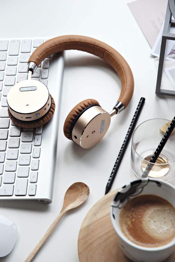 A pair of gold and brown headphones resting on a white keyboard next to a cup of coffee and a spoon.