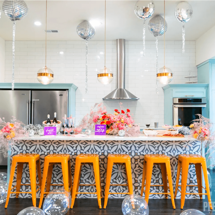 A vibrant kitchen features an ornate bar with orange stools, festive decorations, and food displays.