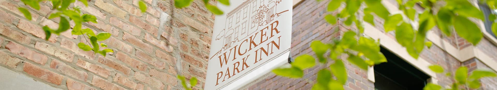 Sign for Wicker Park Inn against a brick wall, framed by green leaves.