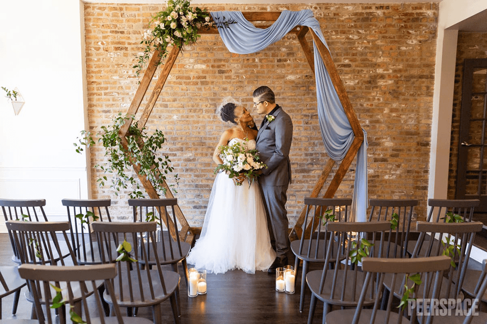A bride and groom embrace under a decorated arch in an intimate ceremony setting.