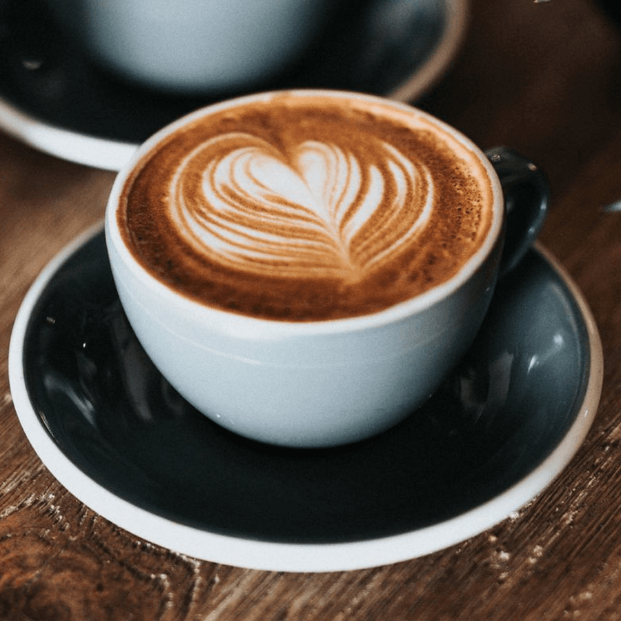 A latte with a heart-shaped foam design in a light blue cup.